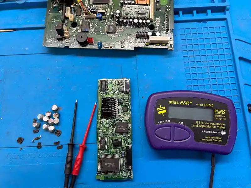 Car radio PCB undergoing capacitor ESR testing during electronic repair service