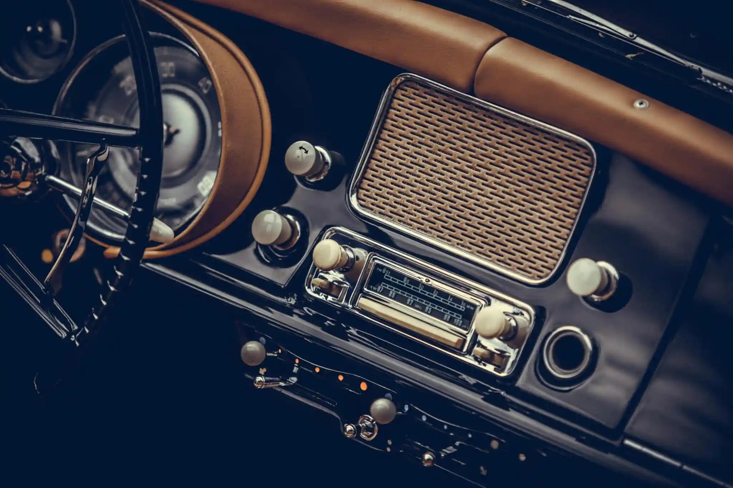 Vintage car dashboard featuring a classic analog radio, speaker grille, and period interior controls.