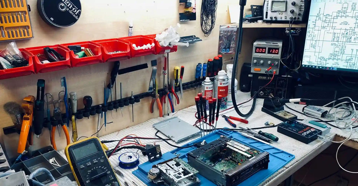 Vintage car radio repair workbench with opened radio unit, diagnostic equipment and electronic tools
